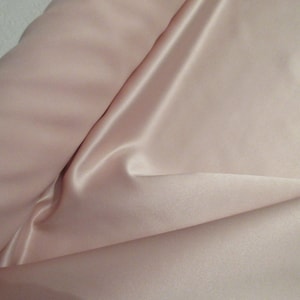 May include: A close-up of a pale pink satin fabric. The fabric is smooth and silky, with a subtle sheen.