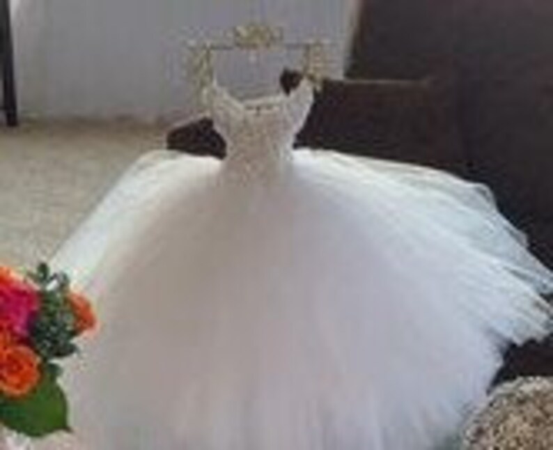 Puede incluir: Un vestido de bola de tul blanco con un corpi&ntilde;o de cuentas y una corona en la parte superior.