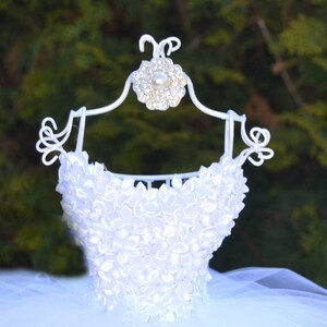 Puede incluir: Tutu de tul blanco con un corpi&ntilde;o de sat&eacute;n blanco decorado con formas de flores blancas. El corpi&ntilde;o est&aacute; en una percha de metal blanco con una flor de pedrer&iacute;a.