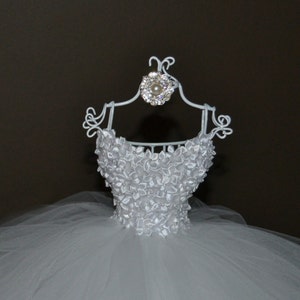 Puede incluir: Vestido de novia de tul blanco en una percha de alambre blanco con un adorno de pedrer&iacute;a y perla.