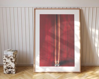 May include: A framed art print featuring two legs in zebra-striped heels against a red backdrop. The artwork is in a wooden frame and leans against a white paneled wall. A marble-patterned side table with a stack of magazines sits nearby.