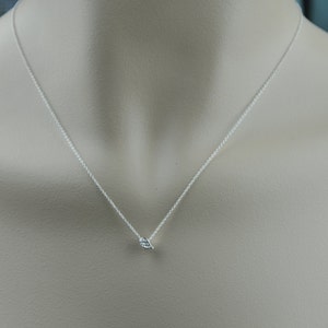Puede incluir: Un delicado collar de plata con un peque&ntilde;o colgante en forma de hoja. El colgante presenta texturas sutiles y cuelga de una fina cadena. El collar se muestra sobre un fondo neutro, destacando su dise&ntilde;o minimalista.