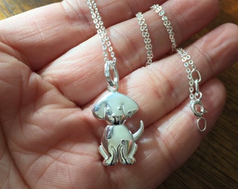 May include: A silver chain necklace with a silver charm of a small dog. The dog is standing on all four paws and has a small tail.