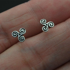 May include: A pair of silver earrings featuring a triple spiral design. The earrings are small and delicate.