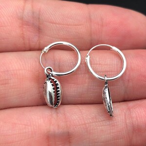 May include: A pair of silver hoop earrings with a small seashell charm hanging from each hoop.