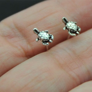 May include: A pair of silver turtle stud earrings. The turtles are facing forward with their heads up and their legs outstretched.