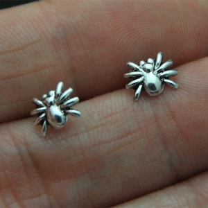 Puede incluir: Un par de pendientes de araña de plata. Las arañas son detalladas y tienen ocho patas.