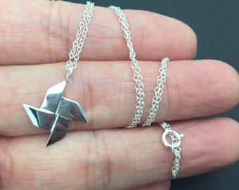 May include: A silver necklace with a silver origami paper windmill pendant. The chain is a delicate, double-strand chain.