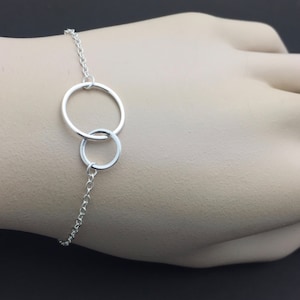 May include: A silver chain bracelet with two interlocking circles. The circles are connected to the chain by a small loop.