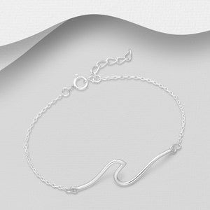 Puede incluir: Un brazalete de cadena de plata con un dije en forma de ola. El brazalete está hecho de una cadena delicada y tiene un cierre de langosta.