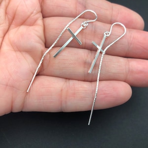 May include: A pair of silver dangle earrings with a delicate chain and a small cross charm.