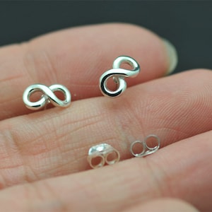 May include: Silver-colored infinity symbol stud earrings. The earrings are small, with a polished finish, and are displayed with their backing pieces. The infinity symbol is a continuous loop, representing eternity and endless possibilities.