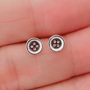 May include: A pair of silver button earrings with four holes in each button.