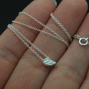 Puede incluir: Un delicado collar de plata con un peque&ntilde;o colgante de ala. El collar tiene una fina cadena y un cierre seguro. El colgante de ala est&aacute; detallado con marcas de plumas individuales. La joya se muestra sobre un fondo oscuro.