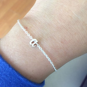 May include: A silver chain bracelet with a small, cursive letter "a" charm.