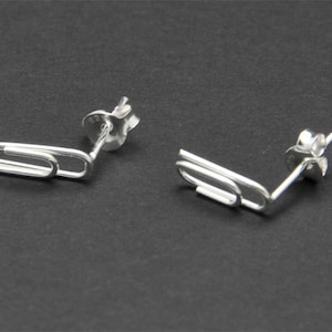 May include: A pair of silver paperclip earrings. The earrings are made of a single piece of wire that is bent into the shape of a paperclip. The earrings are simple and elegant.