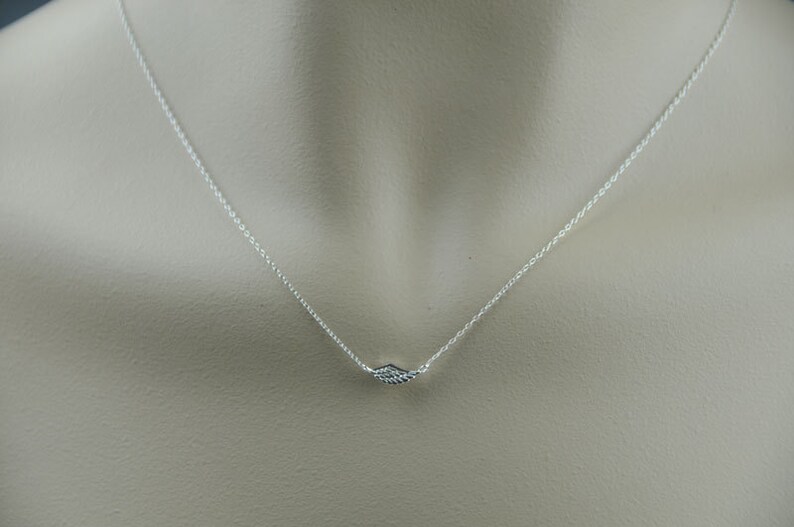 May include: A silver chain necklace with a small, delicate wing pendant.