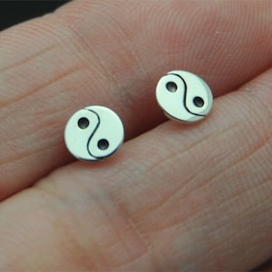 Op de afbeelding: Een paar zilveren yin yang oorbelletjes. De oorbelletjes zijn klein en rond, met een zwart en wit yin yang symbool op elk.
