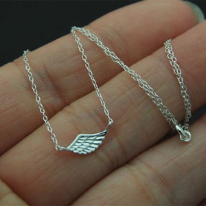 May include: A silver chain necklace with a delicate wing pendant. The chain is a simple, thin chain and the wing is a small, detailed design.