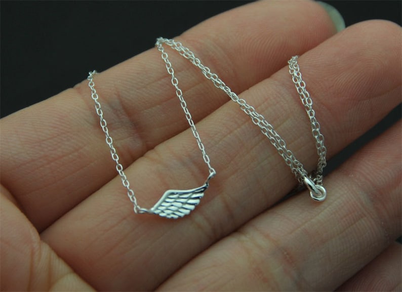 May include: A silver chain necklace with a delicate wing pendant. The chain is a simple, thin chain and the wing is a small, detailed design.