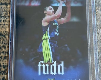 May include: A sports trading card featuring a basketball player in a dark blue and neon green uniform shooting a basketball. The card displays the text RYAN FORS, FUDD, AZZI, and GUARD, along with a WINGS logo, all encased in a clear plastic sleeve.