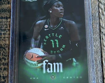 May include: A sports trading card featuring a basketball player in a black Seattle Storm jersey with green lettering, holding a Wilson basketball. The card includes the text RYAN FORS, fam, and AWA CENTER, encased in a clear protective plastic sleeve.
