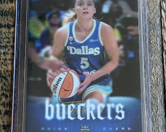 May include: A sports trading card featuring a basketball player in a blue Dallas jersey with the number 5, holding a Wilson basketball. The card displays the text RYAN FORS, bueckers, PAIGE, and GUARD, along with a Dallas Wings team logo.
