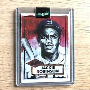 May include: A vintage-style baseball card featuring Jackie Robinson in a white uniform with a blue cap and a red background. The card has a gold border and the text "Jackie Robinson" in a gold marquee.