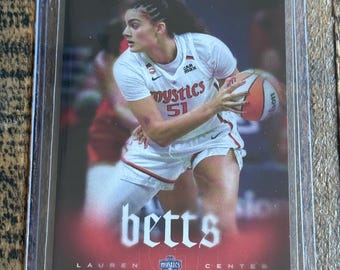 May include: A sports trading card featuring a basketball player in a white Mystics jersey with the number 51, holding a basketball. The card displays the name betts, the text LAUREN CENTER, and RYAN FORS DESIGN, all encased in a clear plastic sleeve.