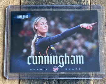 May include: A sports trading card featuring a photograph of a basketball player pointing, encased in a clear plastic protective sleeve. The card displays the text RYAN FORS, CUNNINGHAM, SOPHIE, and GUARD, with a dark blue and black colour scheme.