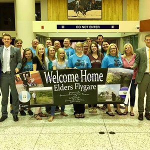 K&ouml;nnte beinhalten: Eine Gruppe von Menschen, die gr&ouml;&szlig;tenteils blaue Hemden tragen, h&auml;lt ein Banner mit der Aufschrift "Welcome Home Elders Flygare Guatemala City East Mission El Salvador 2017-2019".