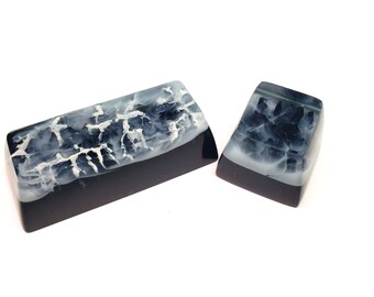 May include: Two resin keycaps with a black base and white marbled design. The larger keycap is rectangular and the smaller keycap is square.