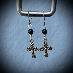 May include: A pair of silver cross earrings with black beads. The earrings have a delicate, ornate design.