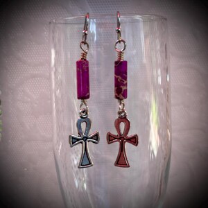 May include: A pair of earrings with a purple and gold stone dangle and a silver ankh charm.