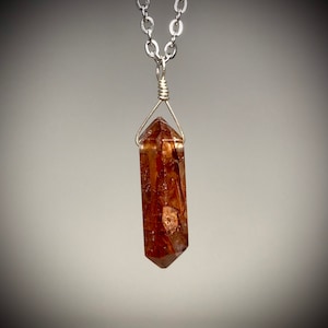 May include: A silver chain necklace with a brown and gold crystal point pendant.