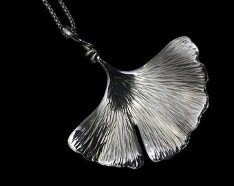 May include: A silver ginkgo leaf pendant necklace with a delicate chain. The leaf is detailed with veins and has a textured surface.
