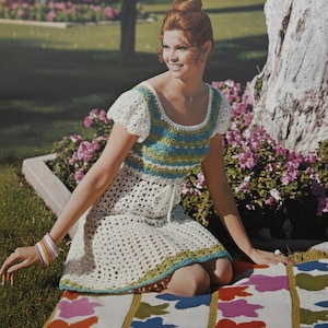 May include: A crochet dress featuring a white base with horizontal stripes in shades of blue and green across the bodice. The dress has short puff sleeves, a scoop neckline, and a tie waist, with a matching blue and green border at the hem.