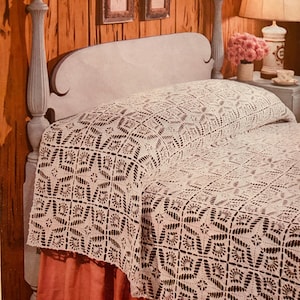 Puede incluir: Un cubrecama de crochet blanco con un delicado patrón floral, drapeado sobre una cama con una cabecera de madera y una falda de cama roja.