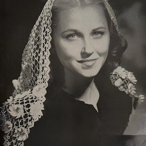 May include: A monochrome portrait of a woman wearing a delicate lace veil with floral embellishments. She is also holding a small bouquet of flowers. The image has a classic, vintage aesthetic, with the woman smiling.