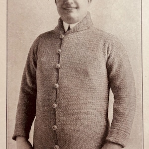 May include: A vintage black and white photo of a man wearing a knitted cardigan with buttons and a cap. The photo is dated 1916.