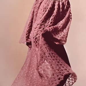 Può includere: Abito all'uncinetto rosa chiaro, in stile vintage, con maniche lunghe svasate e gonna fluida. L'abito presenta un motivo traforato ed è abbinato a collant scuri e tacchi marroni. Un cappello scuro completa il look.