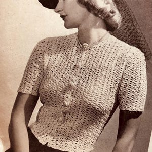 May include: A vintage-style, cream-colored, short-sleeved crochet top with a button-up front. The top features a delicate, openwork pattern. The woman is wearing a black hat with a veil and a pearl necklace. The image has a sepia tone.