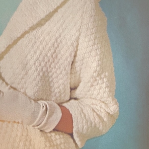 May include: A cream-colored textured cardigan with long sleeves and a folded collar. The fabric features a distinct raised, bumpy pattern throughout the garment. The cardigan has a relaxed fit with cuffed sleeves and a soft, knit-like appearance.
