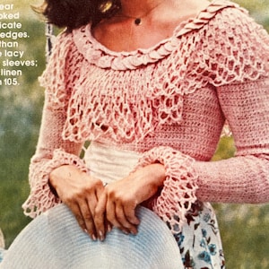 Puede incluir: Una mujer lleva una blusa de crochet rosa con un cuello y puños de crochet blanco. Lleva un sombrero de paja blanco con un borde de crochet. Lleva una falda de estampado floral.