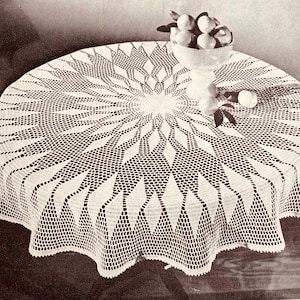 Könnte beinhalten: Weißes gehäkeltes Tischtuch mit einem Sonnenstrahl-Design. Das komplizierte Muster weist einen zentralen Kreis mit radialen Linien und Rautenformen auf. Auf dem Tisch steht eine Glasschale mit Orangen.