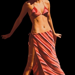 May include: A crochet bikini top and wrap skirt set in shades of red, pink, and orange. The bikini top is a triangle style. The wrap skirt features diagonal stripes. The set is ideal for beachwear or summer fashion.
