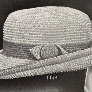 May include: A vintage-style crochet hat in shades of gray, featuring a rounded crown and a wide brim. A darker gray band encircles the hat, with a decorative crocheted element on the side. The number "1114" is printed on the bottom.