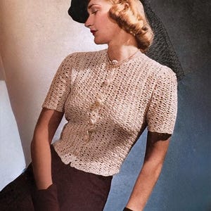 May include: A vintage-style photograph features a woman wearing a cream-colored, short-sleeved crochet top with a button-up front. She is also wearing a black hat with a veil, a pearl necklace, and dark gloves. The skirt is dark brown.