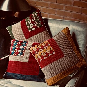 May include: Three crocheted throw pillows with geometric patterns in red, yellow, blue, green, and white. The pillows are arranged on a white couch.