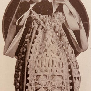 May include: A vintage-style crocheted drawstring bag with a floral pattern and decorative edging. The bag is cream-colored and features a dark brown circular backing with two cream-colored ribbons tied in bows. The bag is likely handmade.